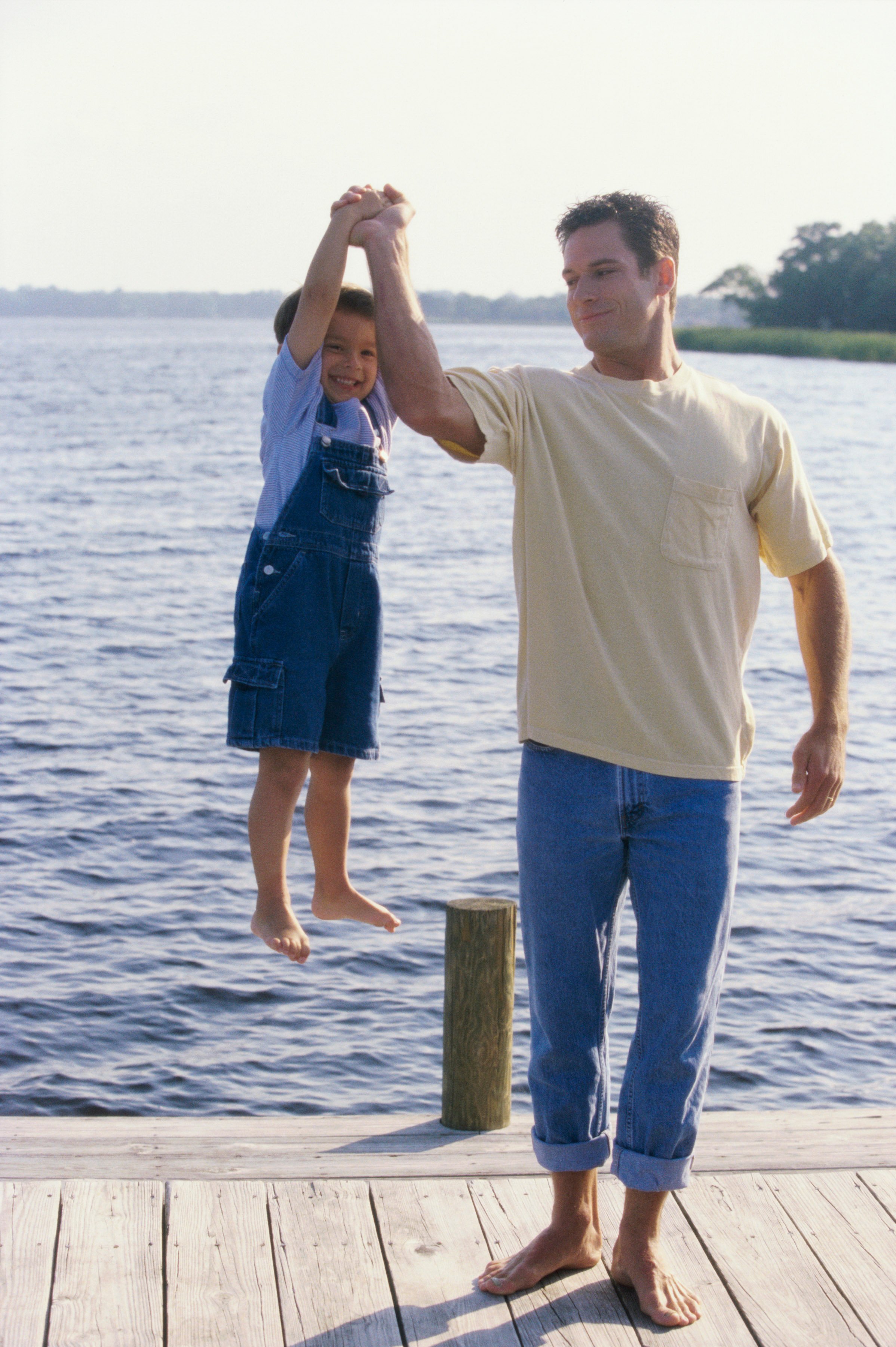 Dad lifting son with one arm on a dock