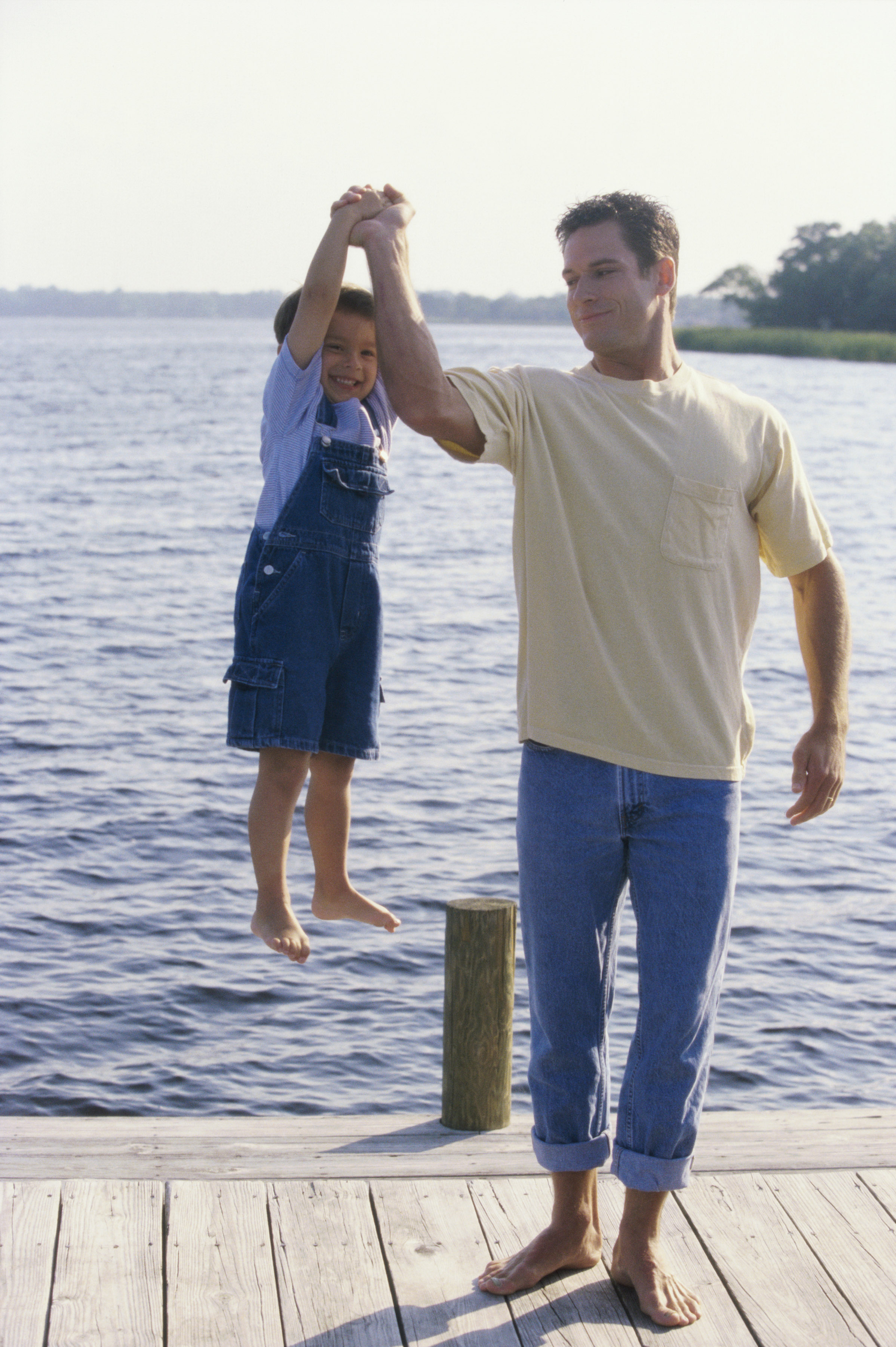 Dad lifting son with one arm on a dock