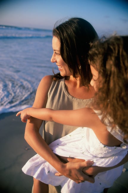 Mother holding daughter while looking at ocean