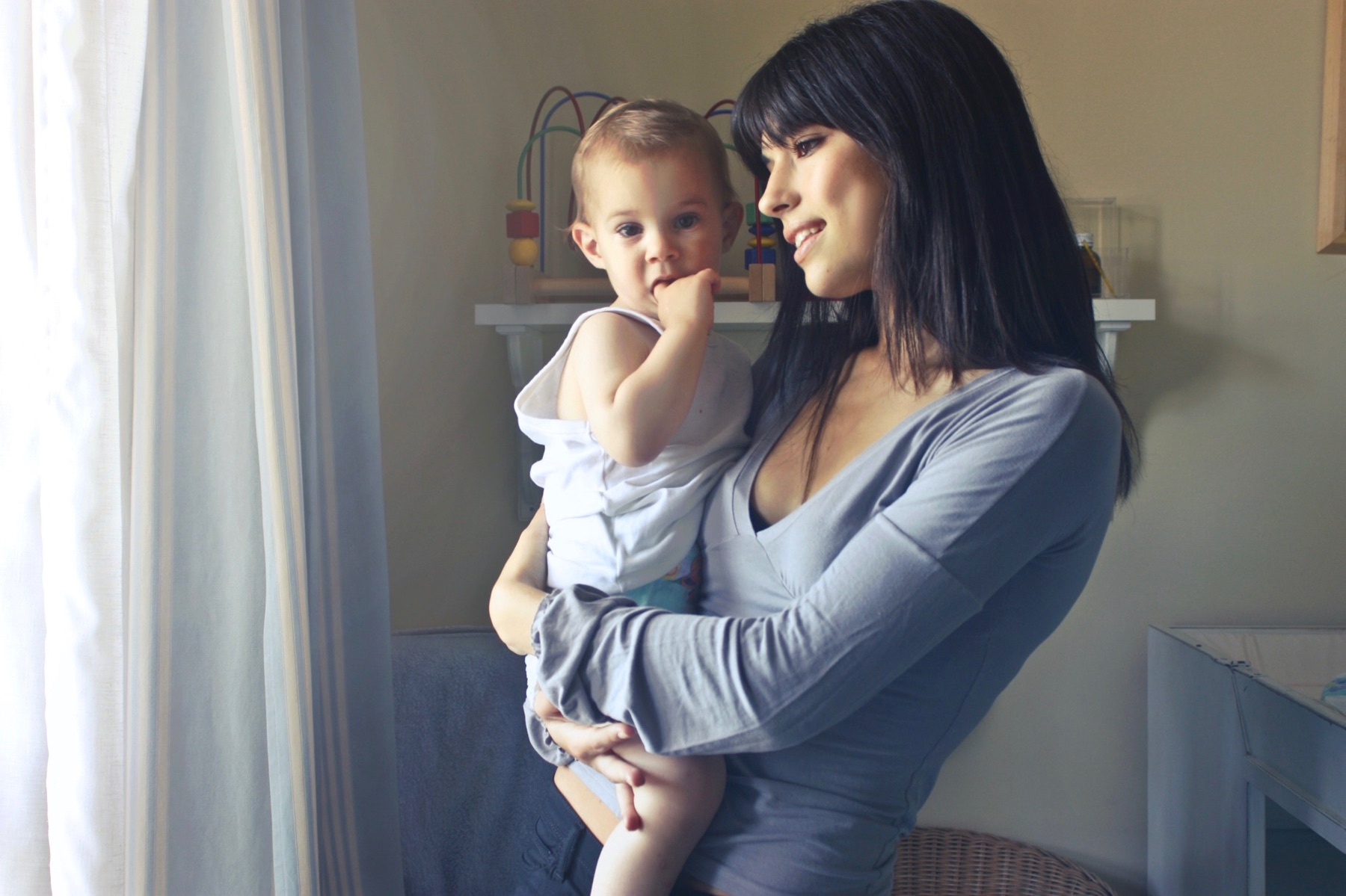 A mother looks out the window as she holds her baby.