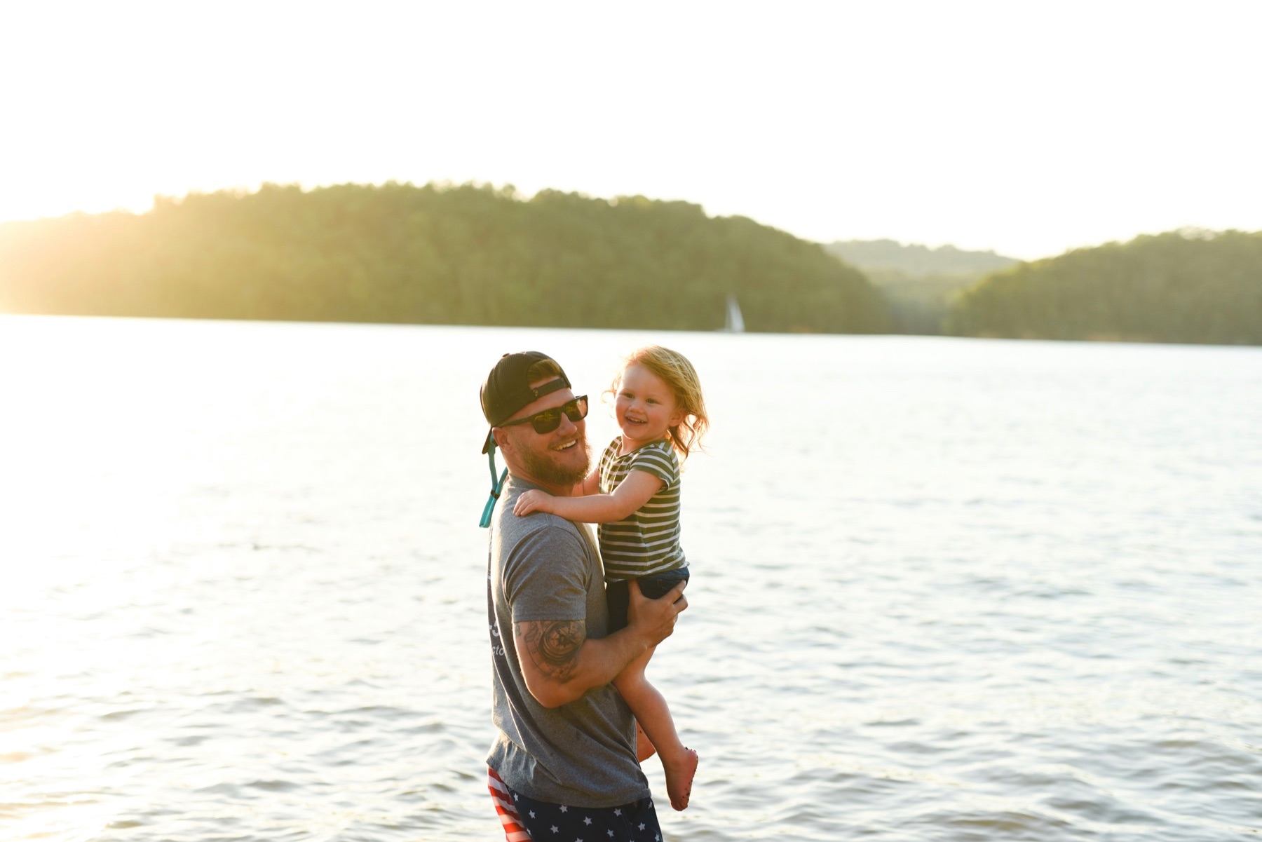 A man and his daughter smile for a photo by the water.