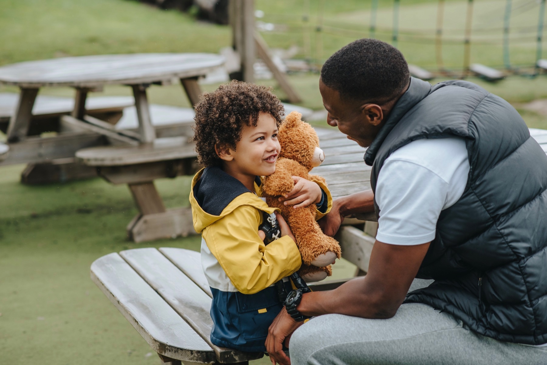 Father and son sit together at a table in the park.