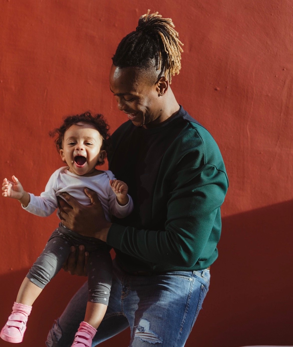 A man smiles as he holds a baby who is also smiling.