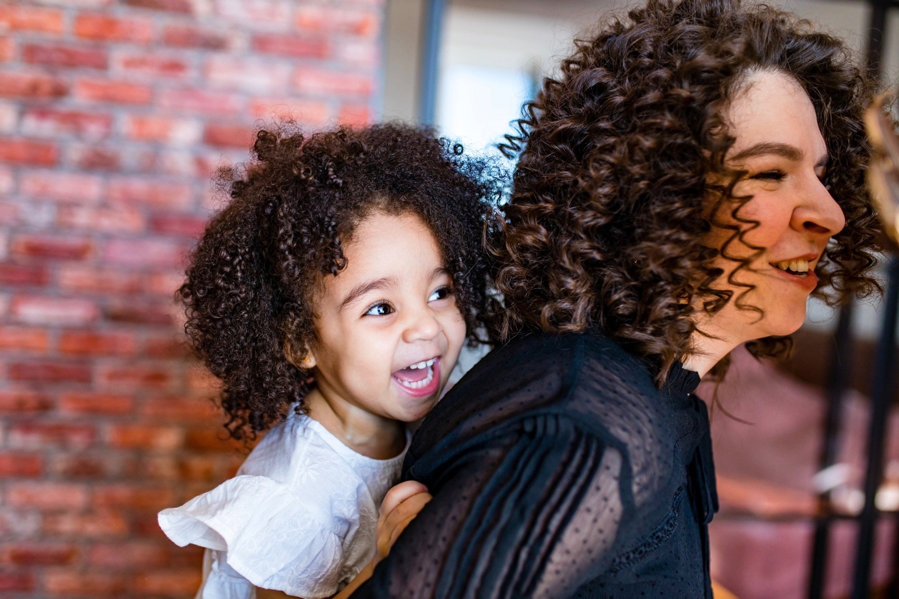 A woman with curly hair gives a toddler a piggy back ride.