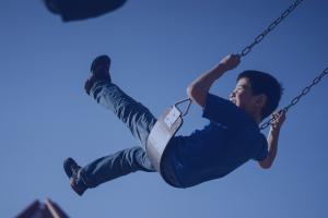 Young boy laughs as he swings outside on a clear spring day.