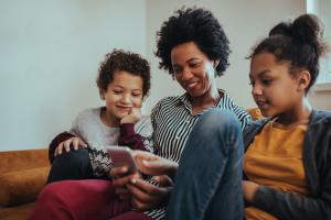A mother sits between her two children as all three look at the smartphone in her hands.
