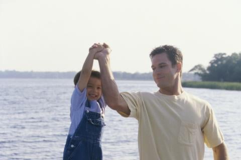 Dad lifting son with one arm on a dock