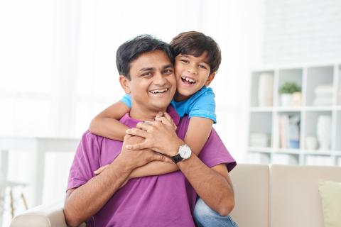 Smiling son hugs doting father from behind