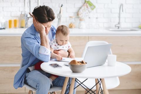 Man sits at his computer desk holding his baby with a disappointed look on his face.