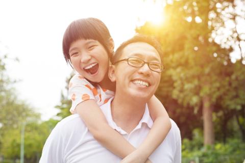 Dad and daughter smile together in the sun.