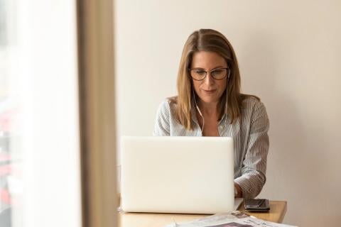 A woman works on her computer by the window.