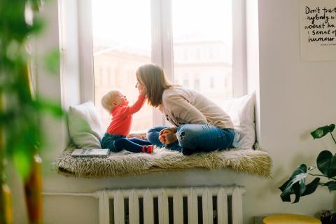 Baby reaches to touch its mother as they sit together at the window