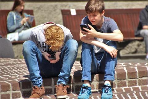 Two boys sit on a step and look at their smartphones.