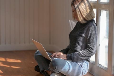 Woman sits near a window to use her computer.