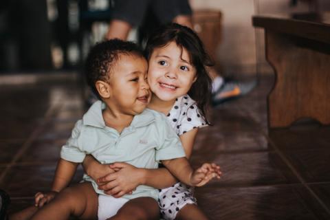 An older sister holds her younger brother in her lap.