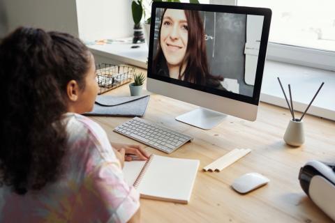 Young girl uses her home computer to have a videoconference with her teacher.