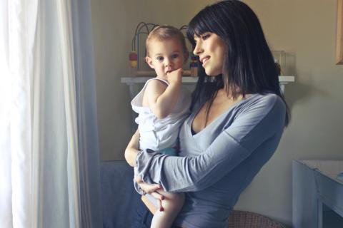 A mother looks out the window as she holds her baby.