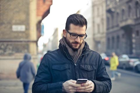 After crossing the street, a man looks at his phone.