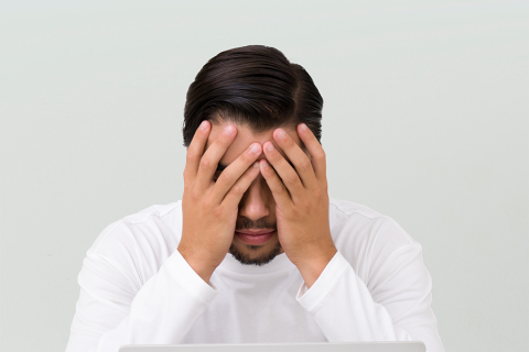 Man sits with his head in his hands in front of his laptop