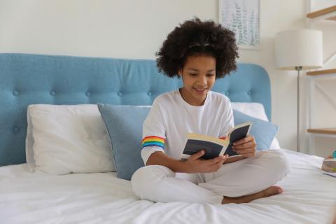 A young girl reads quietly in bed.
