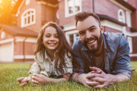 Dad and daughter smile for a photo in the grass in front of a house.