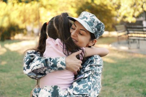 Woman in a military uniform happily embraces a young girl.