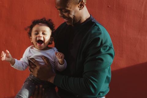 A man smiles as he holds a baby who is also smiling.