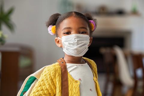 A young girl wearing a face mask and a backpack poses for a photo.
