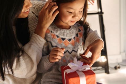 A young girl sits in her mothers lap as she receives a holiday gift.