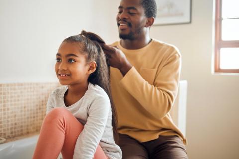 A father braids the hair of his young daughter.