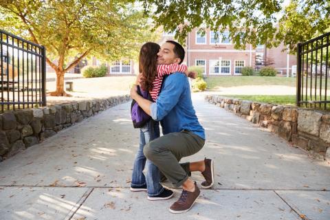 Dad hugging daughter on sidewalk. 