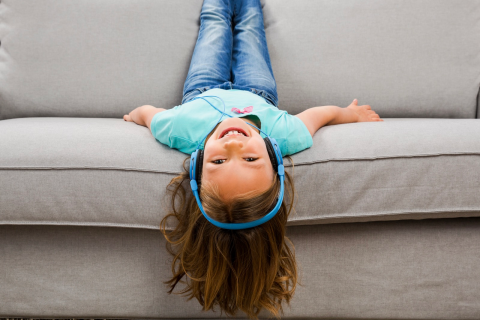 Girl laying upside on couch wearing headphones.