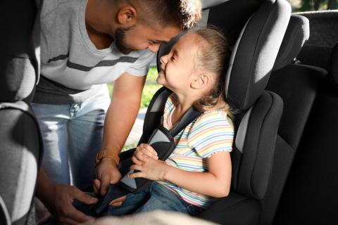 Man buckling his daughter into carseat. 