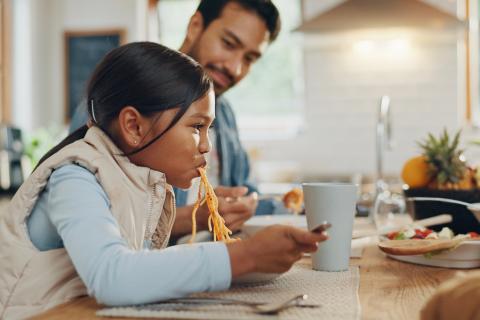 Dad and daughter eating spaghetti.