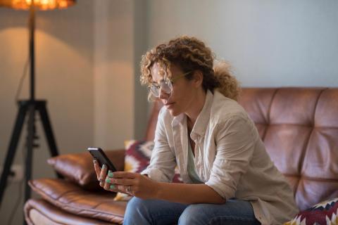 Woman on couch, looking at her phone seriously.