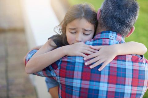 Young girl hugging her dad while looking upset.