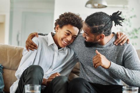 Dad and son on couch talking happily.