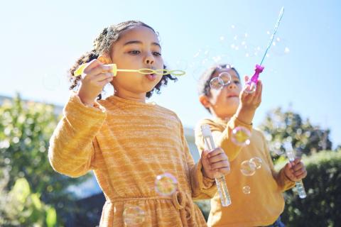 Young siblings playing with bubbles outside.