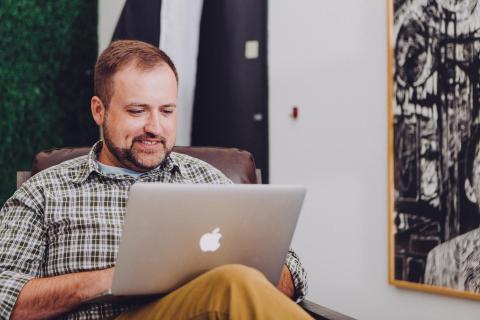 A man sits in an office using a laptop computer.