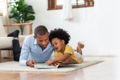 Dad and young child reading a book on floor. 