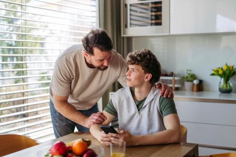 Man talking to teenage boy in kitchen.