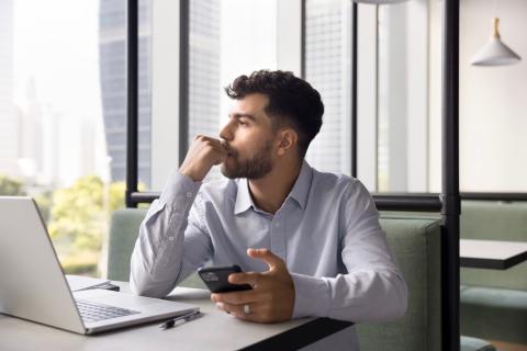 Man holding his phone and thinking, with a pensive look on his face. 