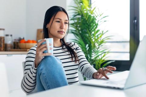 Woman drinking tea while considering response to message.
