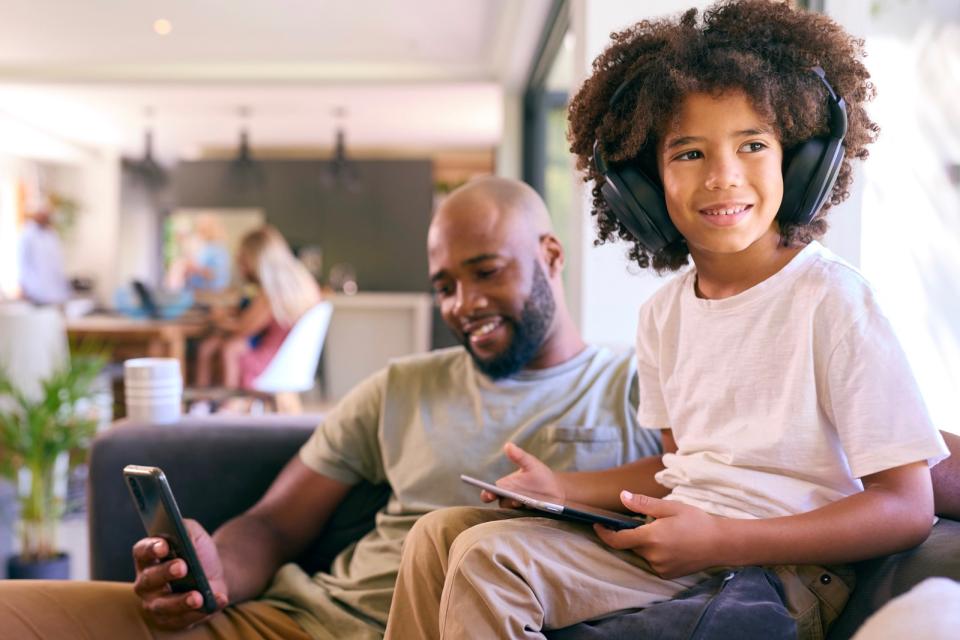 Young boy wearing headphones while sitting with his dad on the couch. 