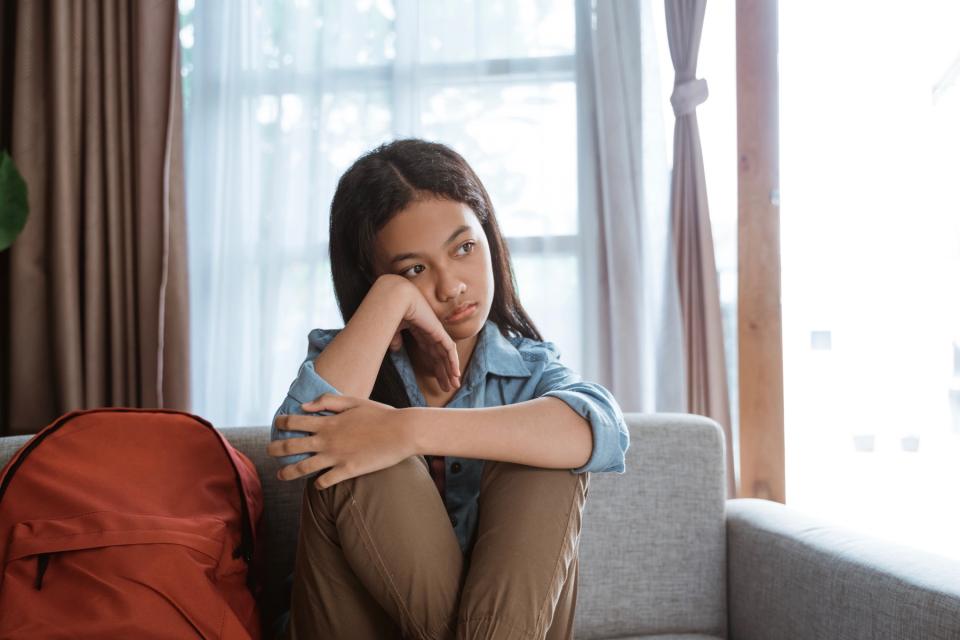 Young girl waiting on couch with her backpack.