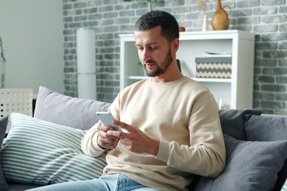 Dad calmly reading text message on couch. 