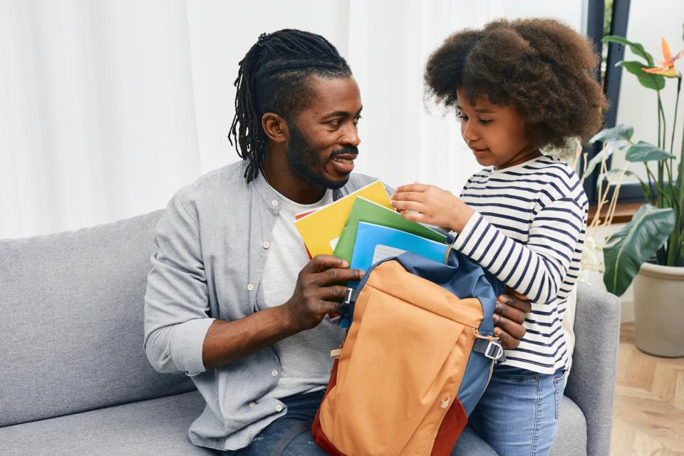 Dad helping young daughter pack her backpack before school.