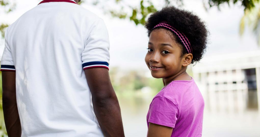Young girl smiles over her shoulder as she holds her father's hand.