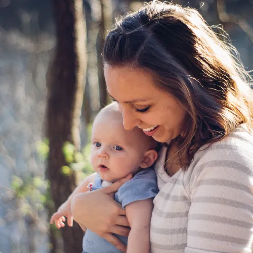 Smiling mother holds young infant outside