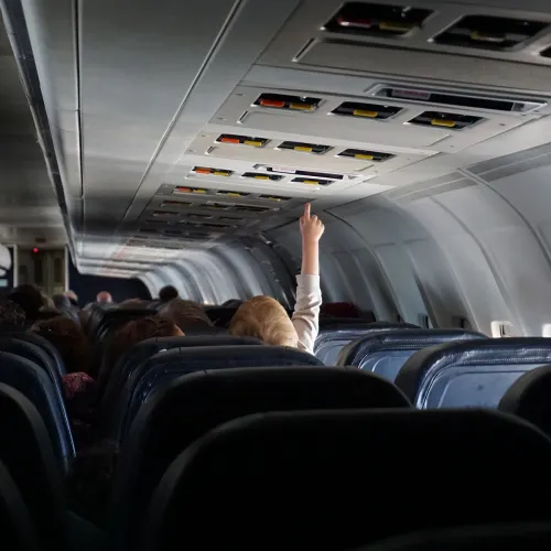 Little boy reaches for the light above him while seated on an airplane.